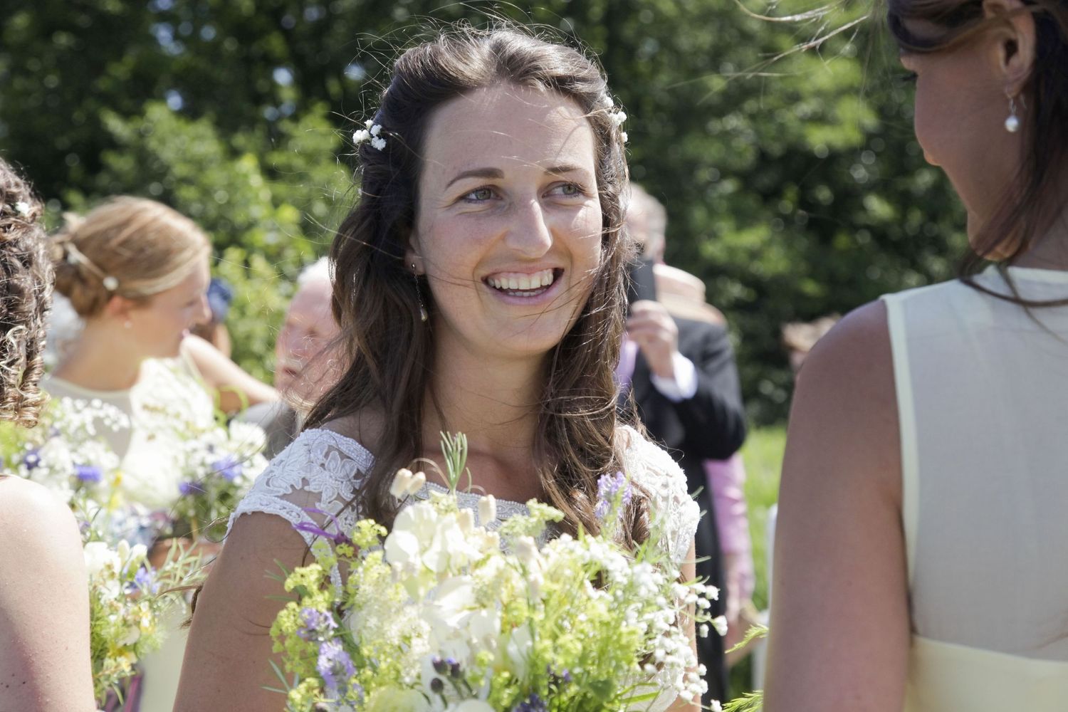 Bridesmaids wearing light-colored dresses hold bouquets while celebrating outdoors.