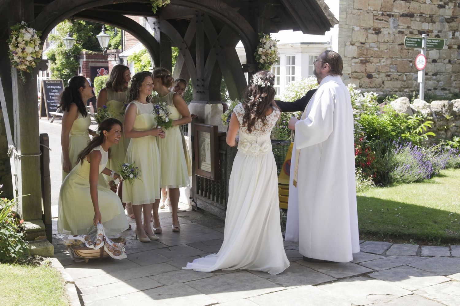 Wedding ceremony under a covered church entrance with bridesmaids in pale yellow dresses.
