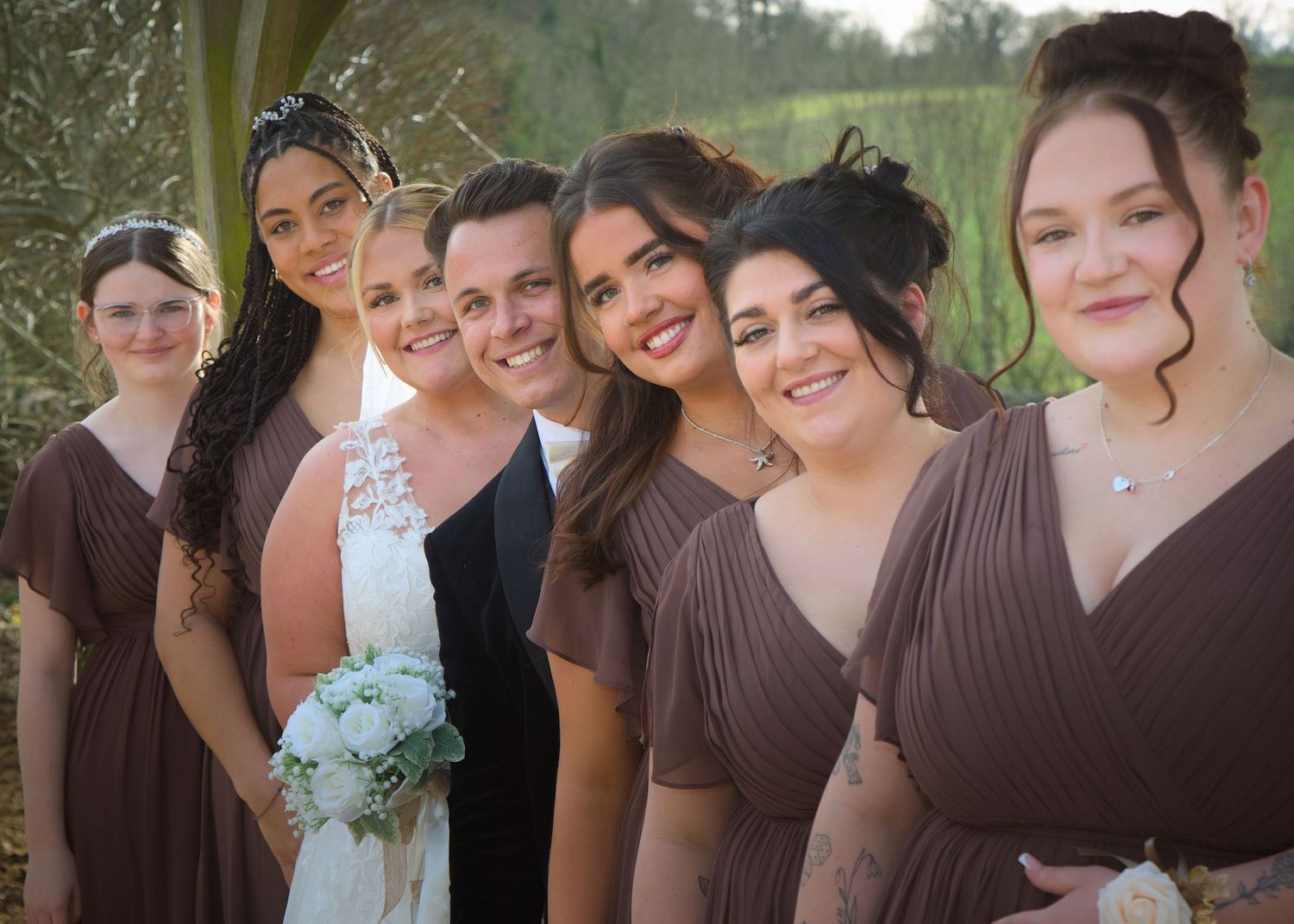 Bridesmaids in chocolate brown dresses pose together at outdoor wedding.