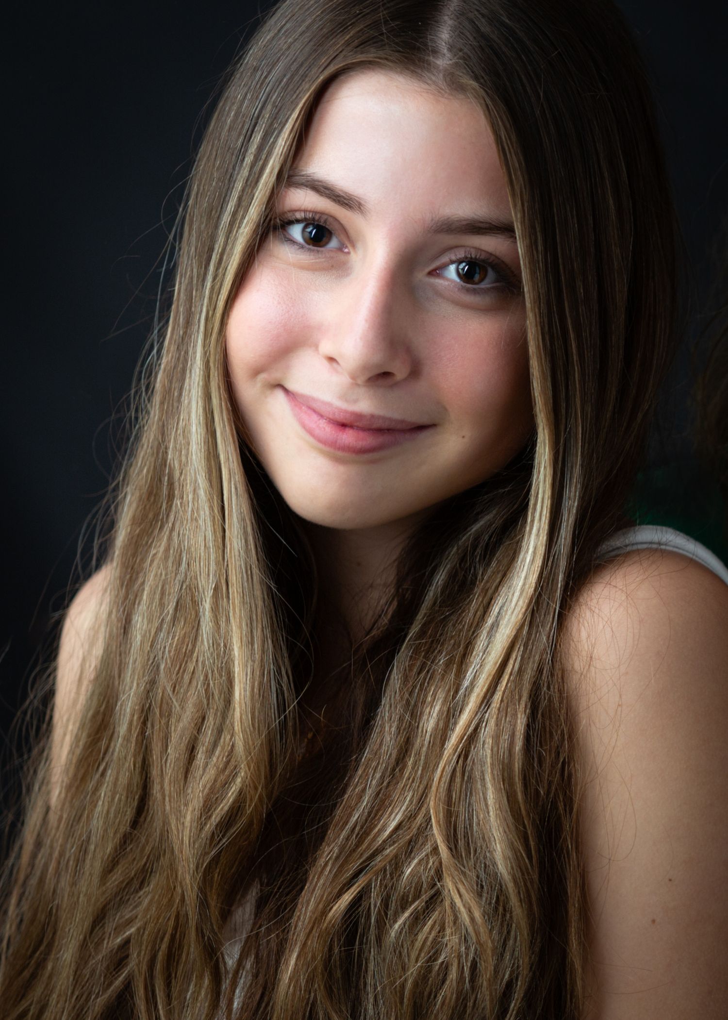 Portrait photo with soft lighting showing long wavy blonde hair and gentle smile against dark background.