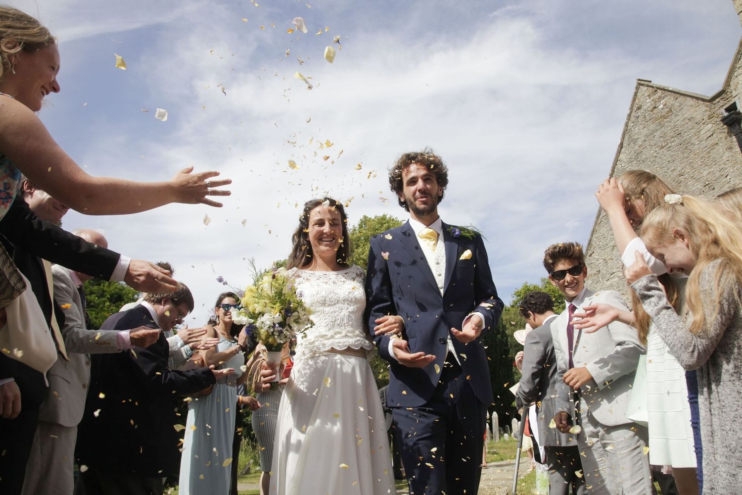 Wedding celebration with guests throwing confetti against blue sky backdrop.