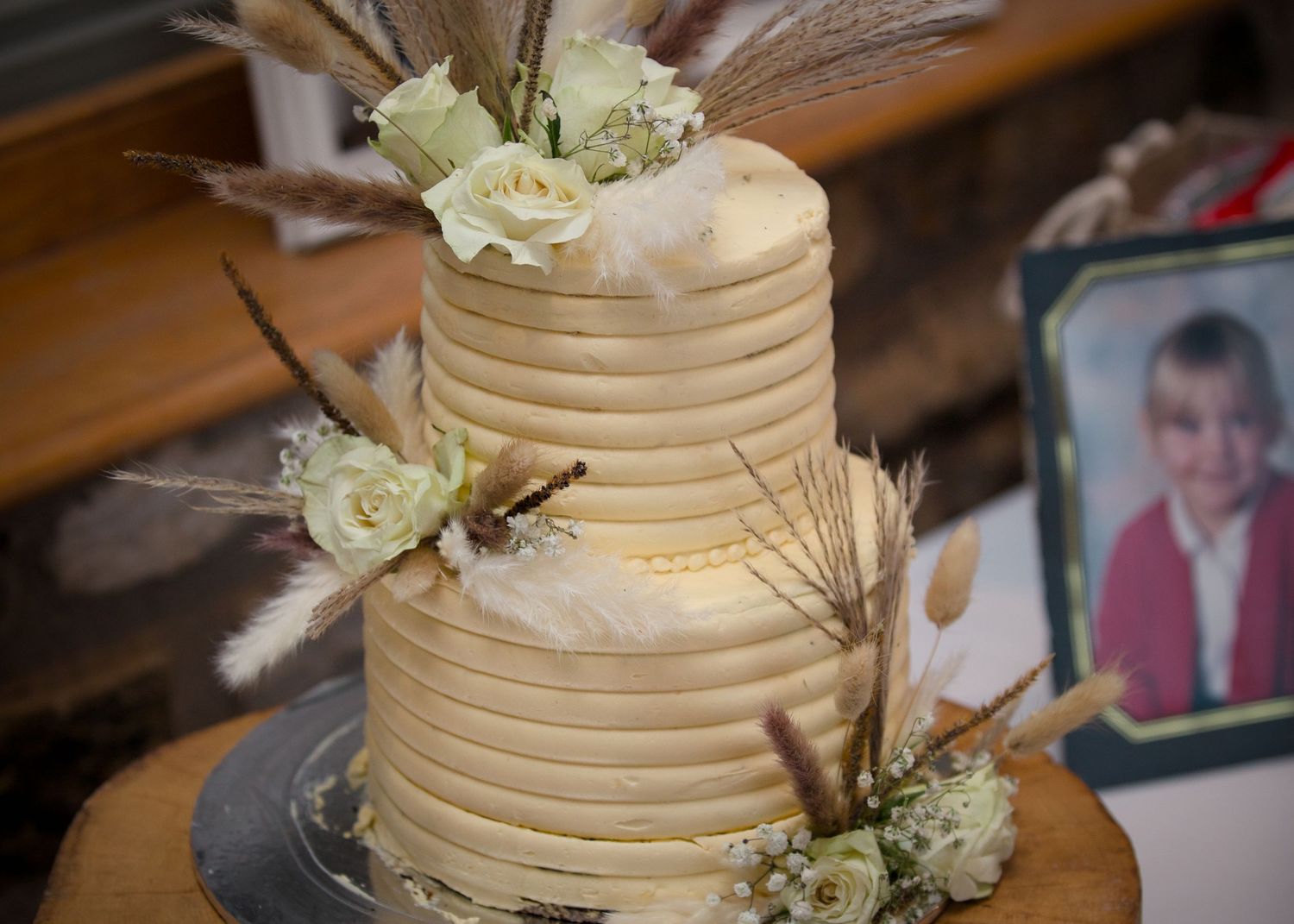Three-tiered cream colored wedding cake decorated with white flowers and greenery.