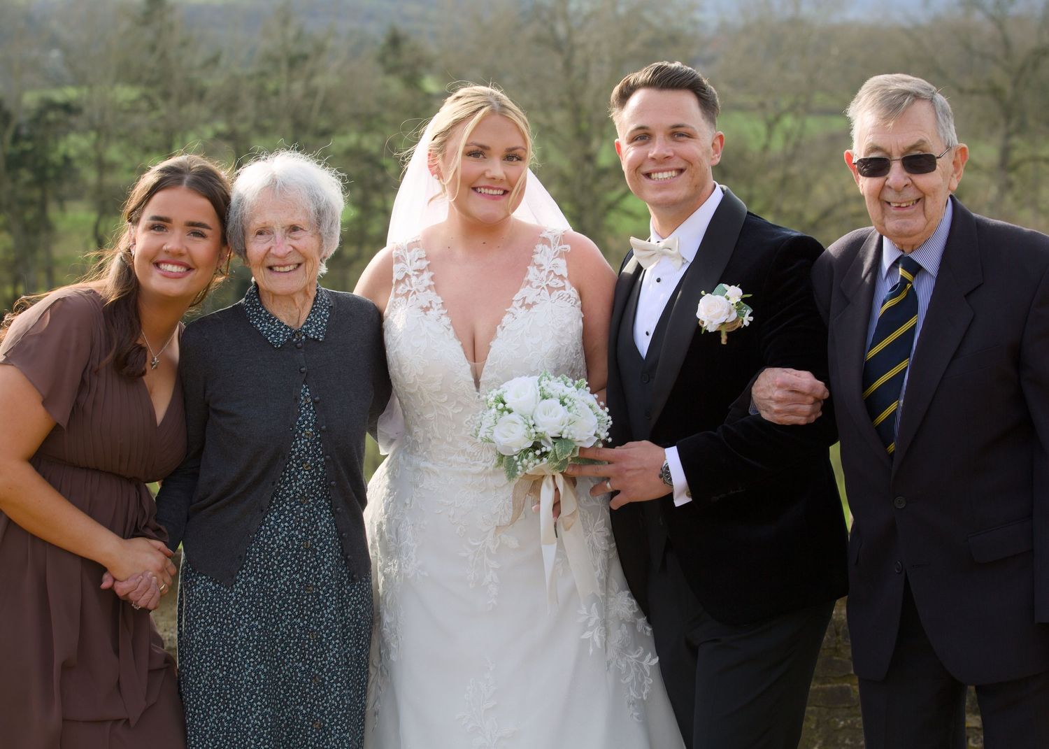 Wedding party group photo with bridesmaids in brown dresses and groomsmen in black suits.