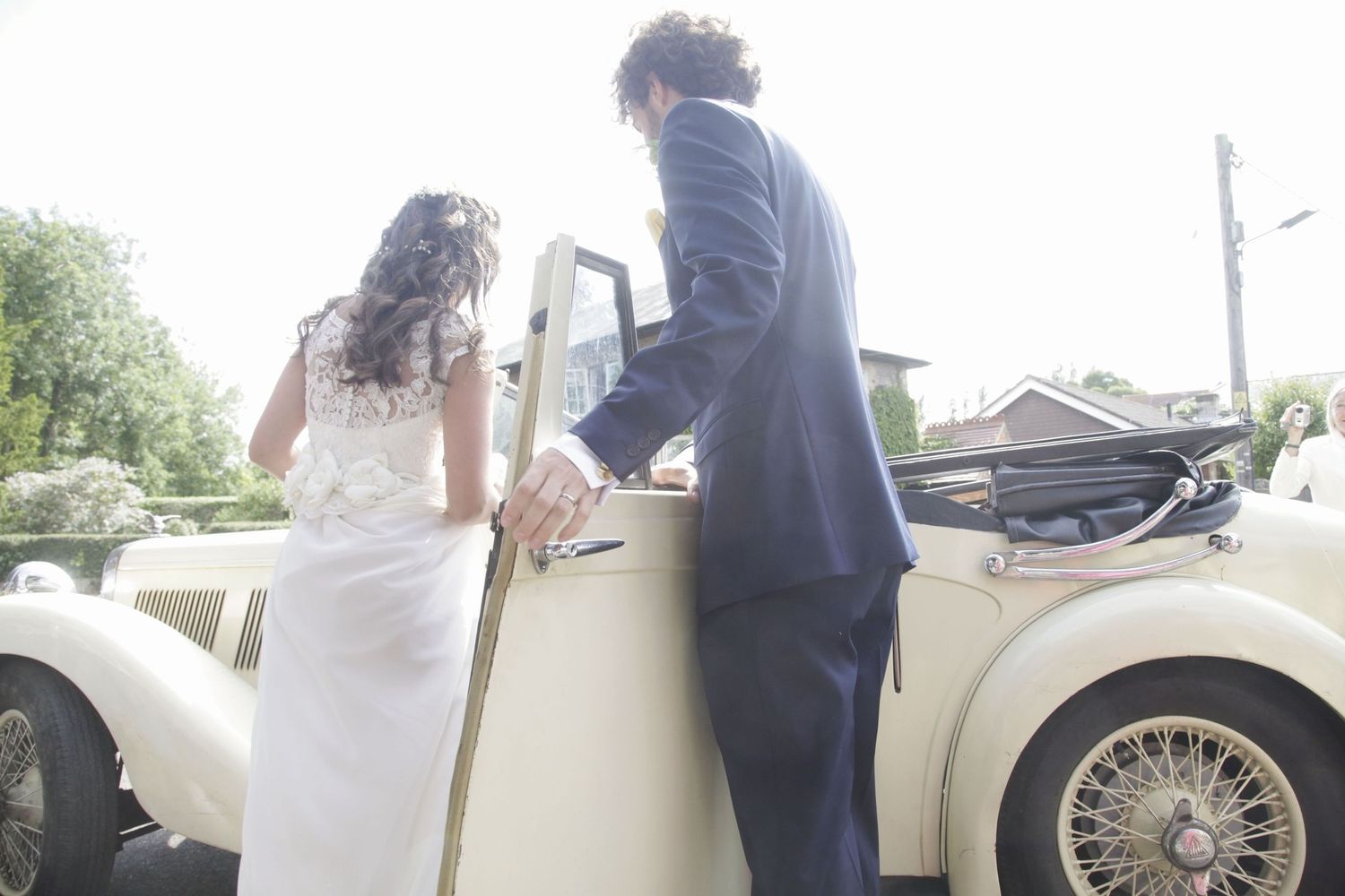 Vintage cream-colored wedding car parked outside stone building.