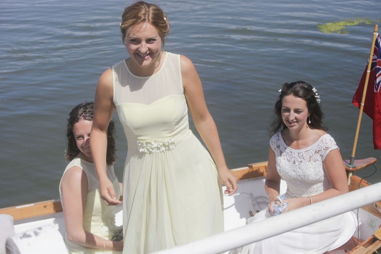 Passengers in light-colored dresses sit aboard a decorated wooden boat on the water.