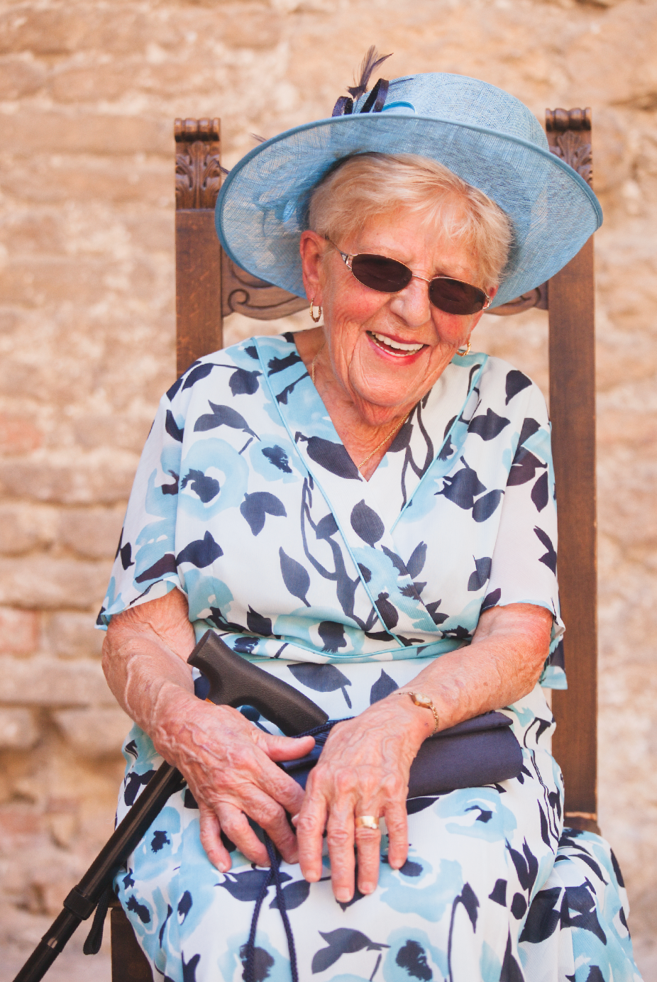 Senior guest in blue floral dress and sunhat enjoying outdoor celebration.