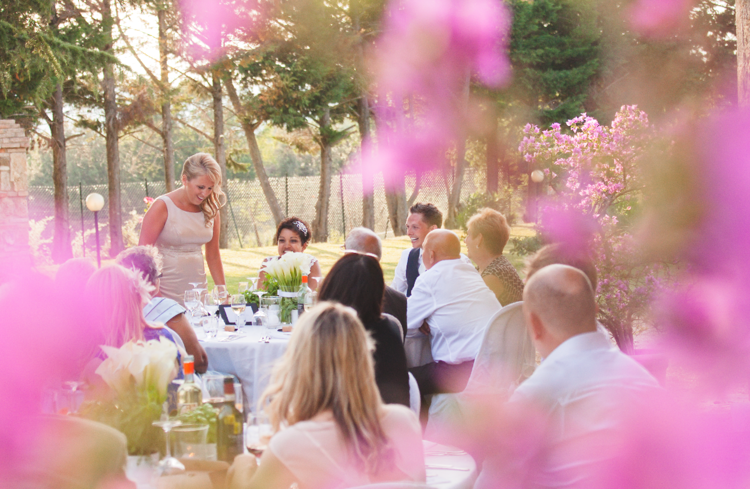 Outdoor wedding reception with pink flowers and natural sunset lighting.