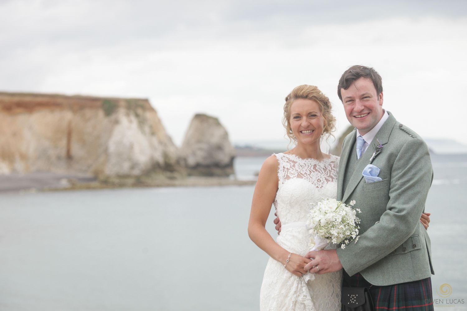 A couple poses together on their wedding day near coastal cliffs.