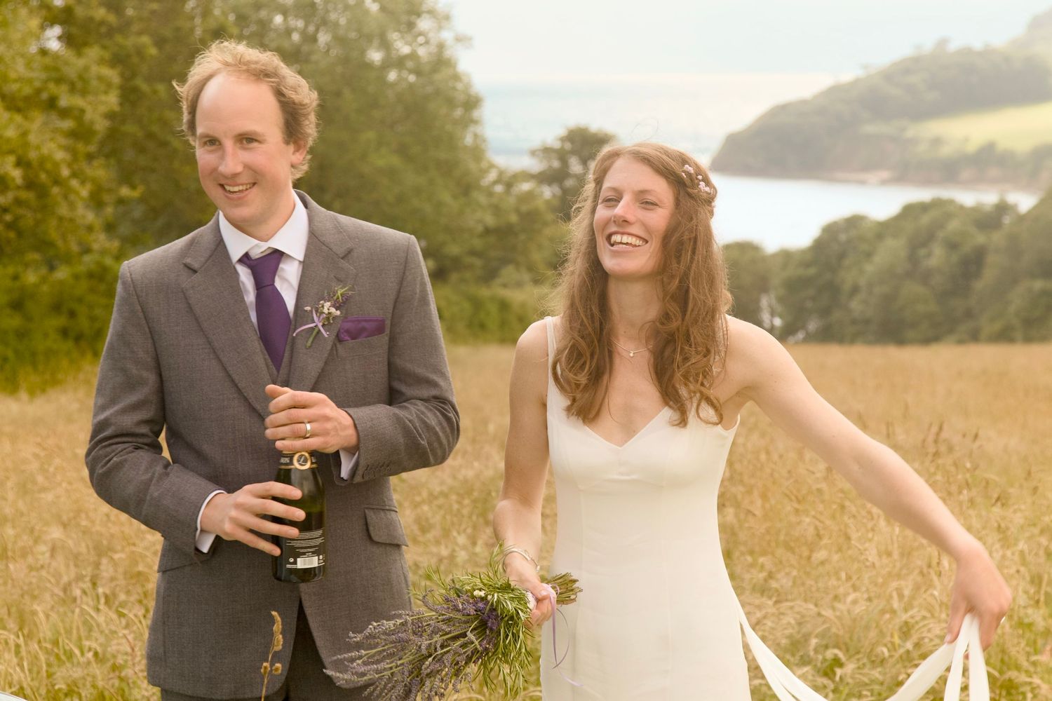 A couple laughs together while standing in a golden sunlit field during a wedding photo session.