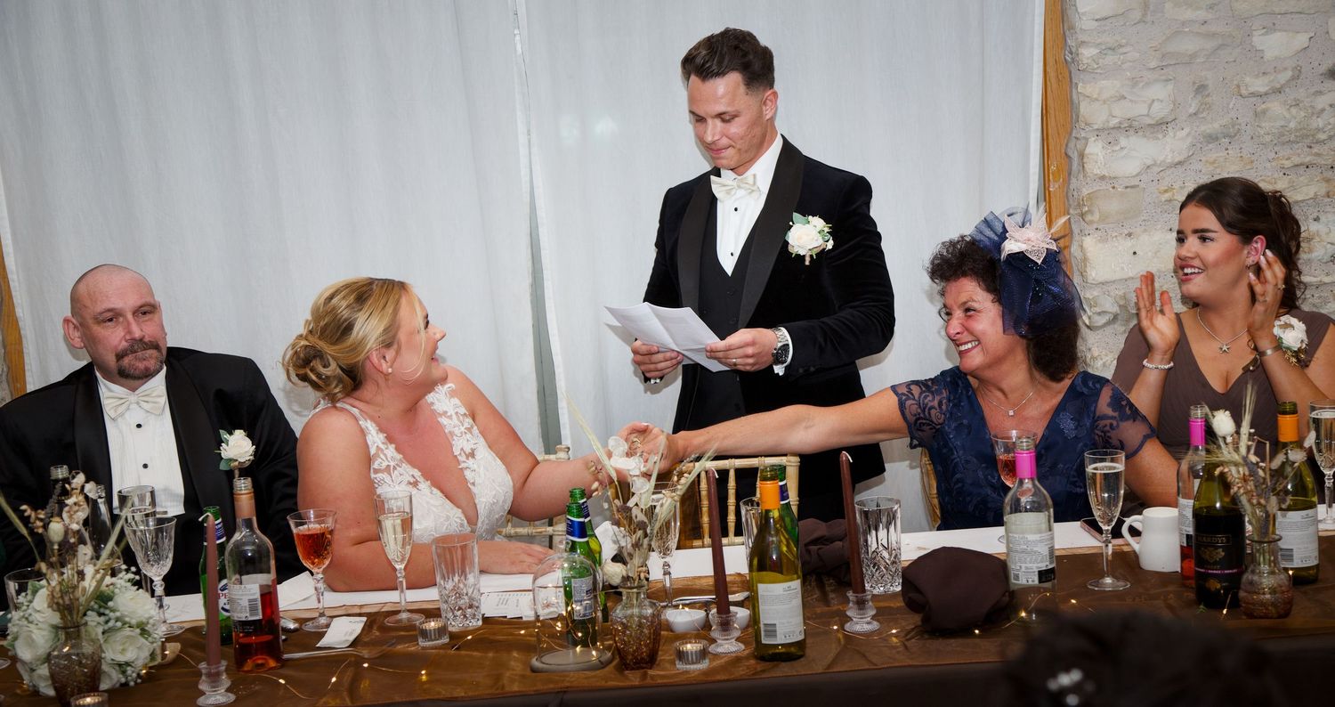 Wedding party seated at long head table during reception celebration.
