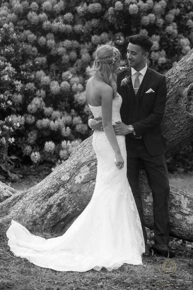 A wedding couple poses against a backdrop of blooming white flowers in a black and white photograph.