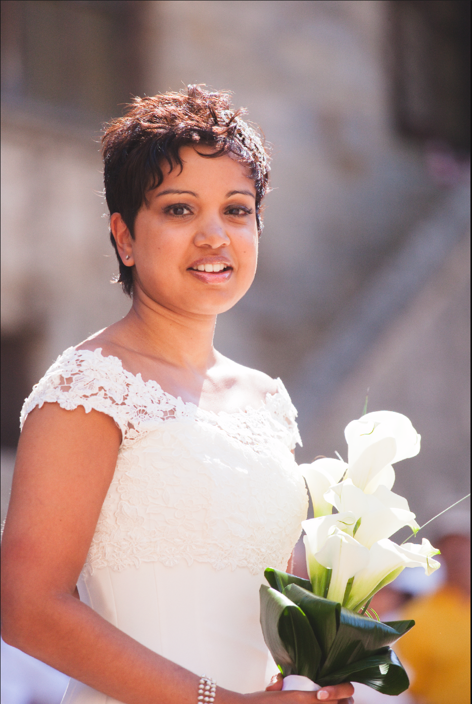 A radiant bride holds white calla lilies while wearing an elegant lace-trimmed gown.