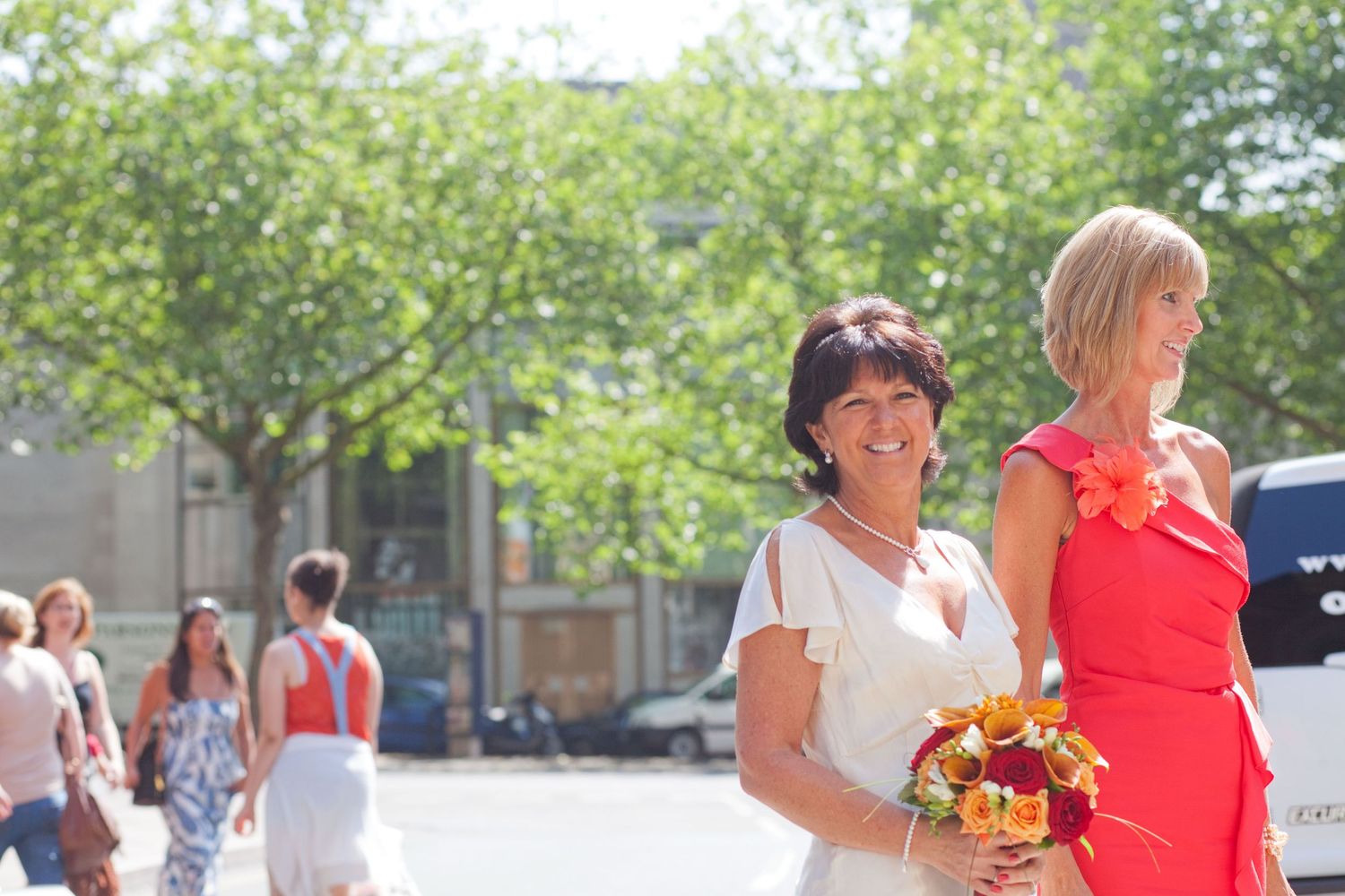 Wedding party walking outdoors on a sunny day with trees and buildings in the background.