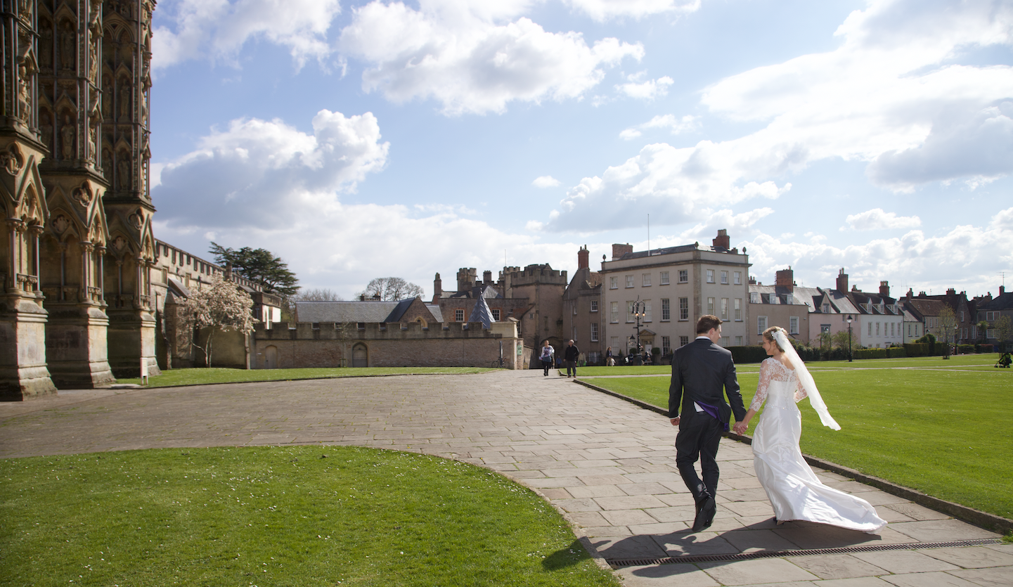A couple walks along a path on their wedding day at Wells Cathedral, Somerset.