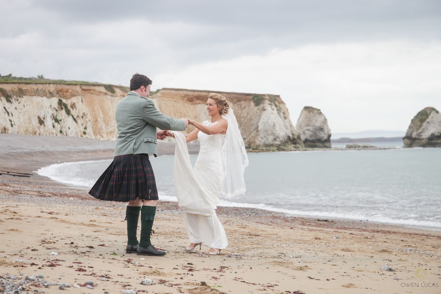 Wedding couple walking along scenic beach with cliffs in background.