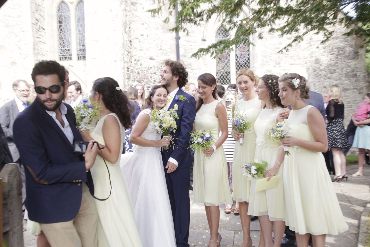 Wedding party in yellow dresses and navy suits mingling outside historic church.