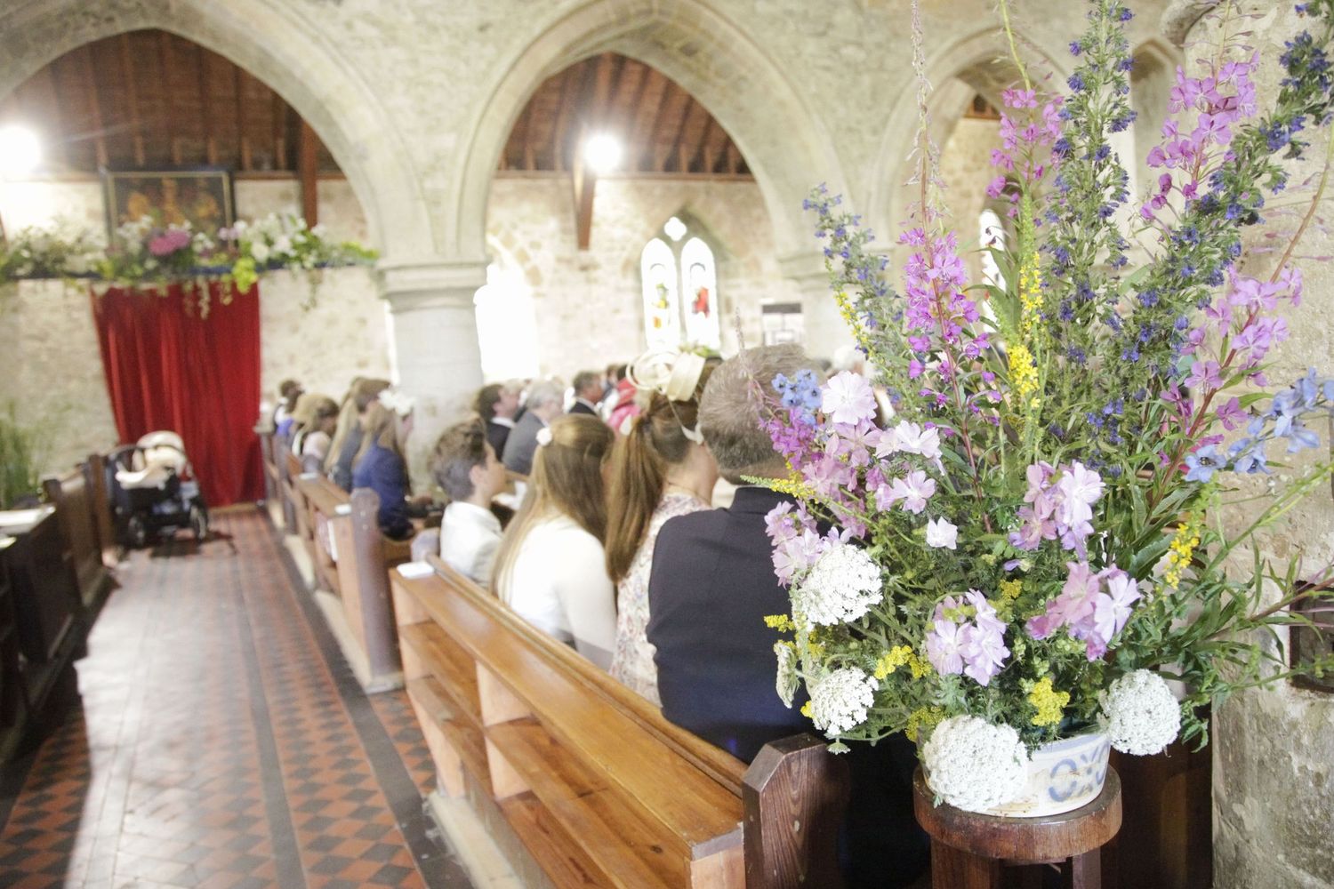 Church interior decorated with purple flowers and wooden pews for wedding ceremony.