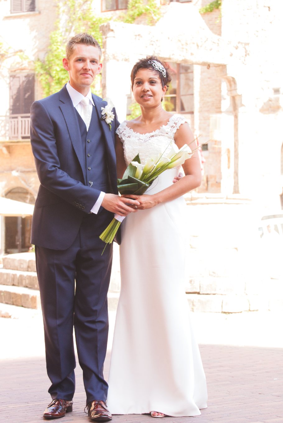 Elegant wedding photo showing couple in navy suit and white dress on cobblestone street.