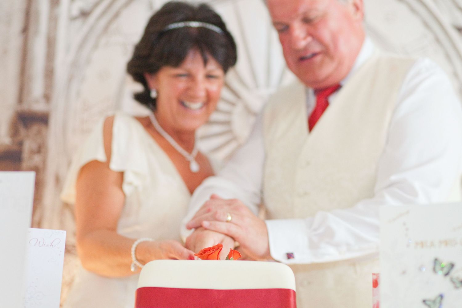 A happy couple shares a joyful moment while cutting their red and white wedding cake.