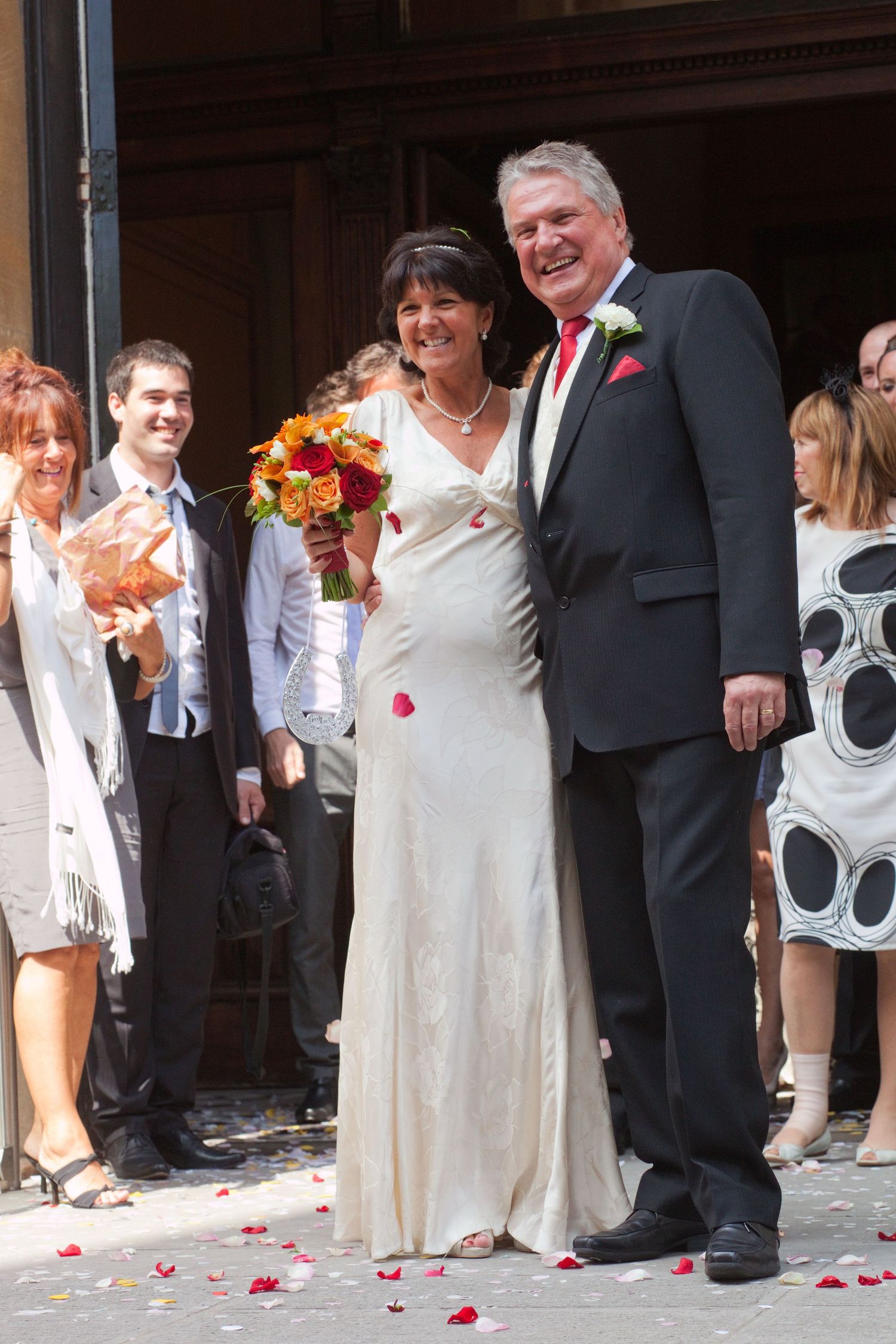 A happy couple posing for photos after their wedding ceremony with rose petals scattered on the ground.
