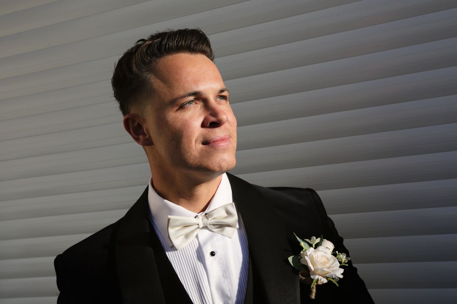 A groom in a classic tuxedo and bow tie smiles against a white background.