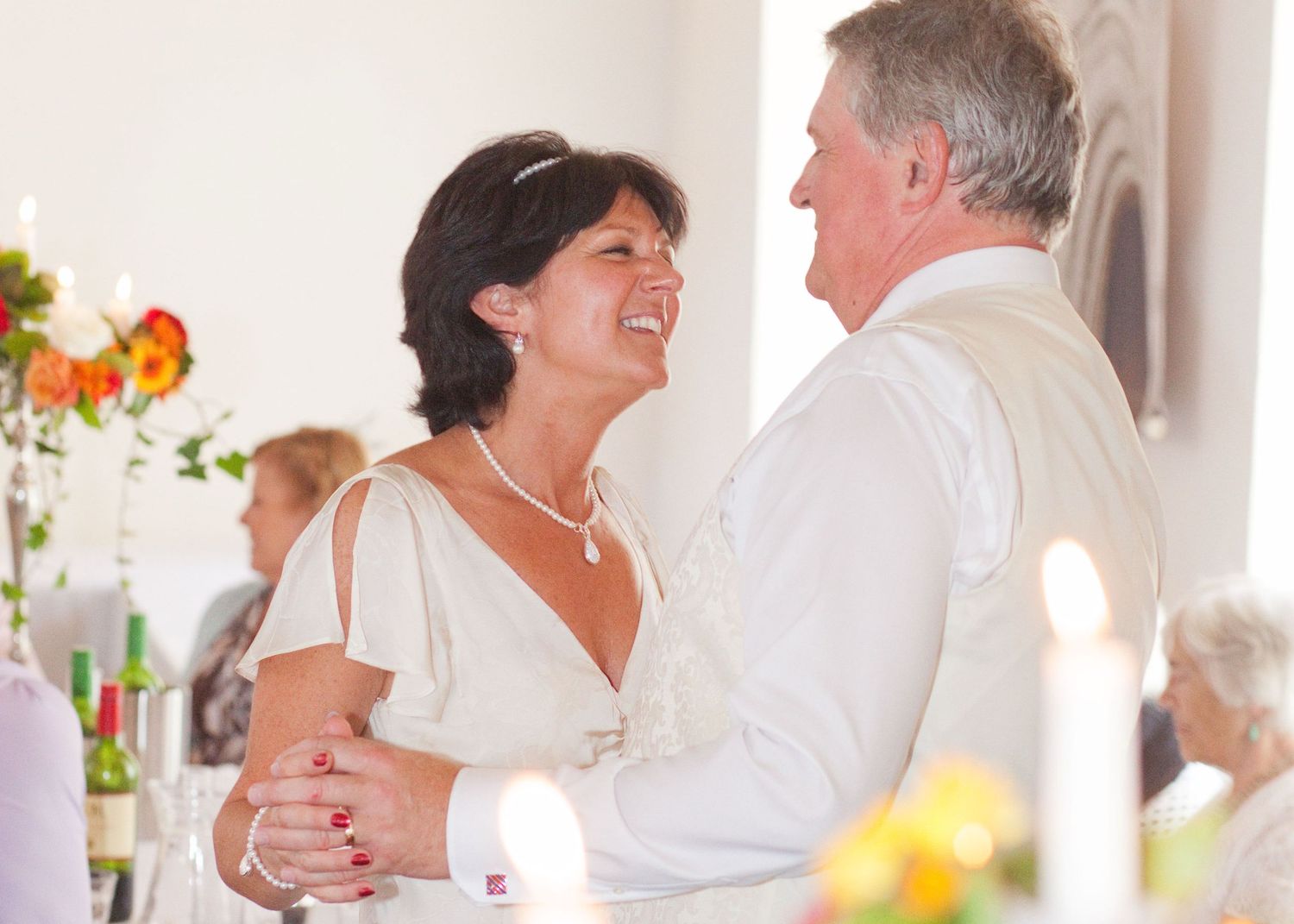 Couples dancing and embracing at a formal celebration in white outfits.