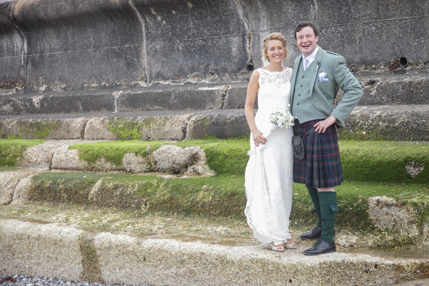 Wedding photography session against a textured stone wall near the coast.