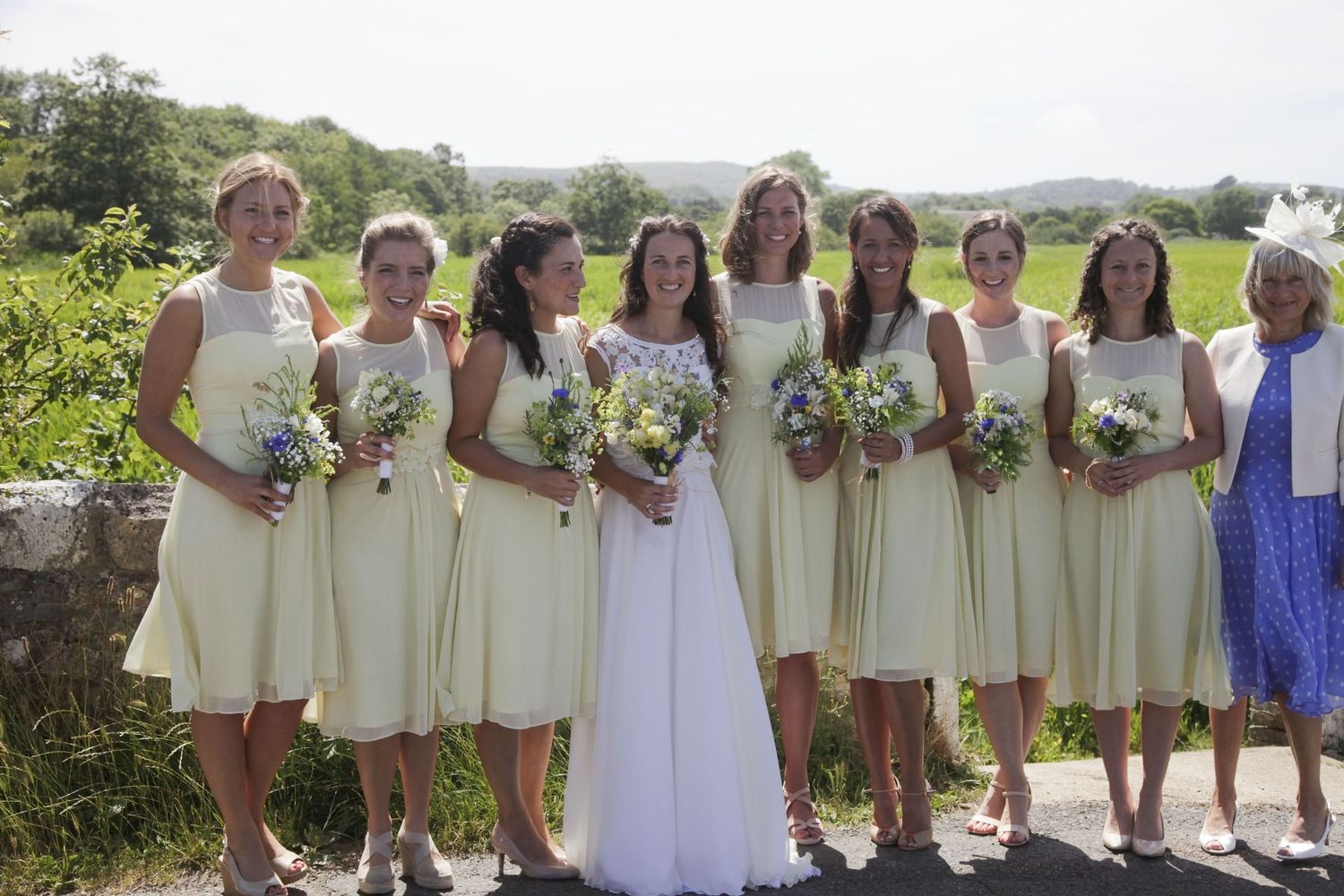 Wedding party members in coordinated cream dresses pose together on a scenic hillside path.