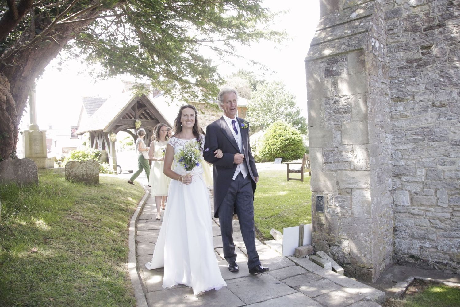 Couple walking along a stone church pathway surrounded by lush greenery.