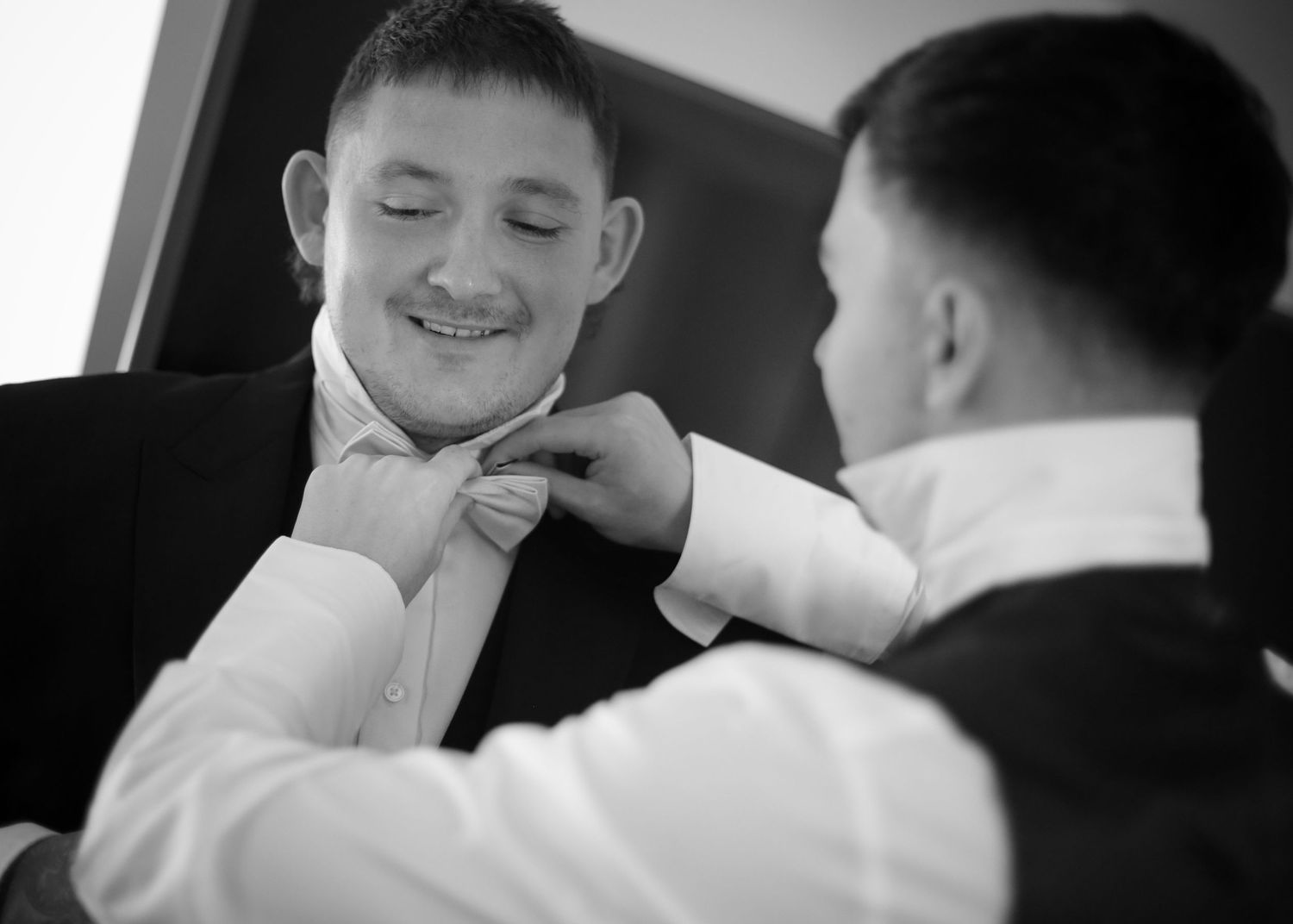 Black and white photo of wedding preparation showing bow tie adjustment.