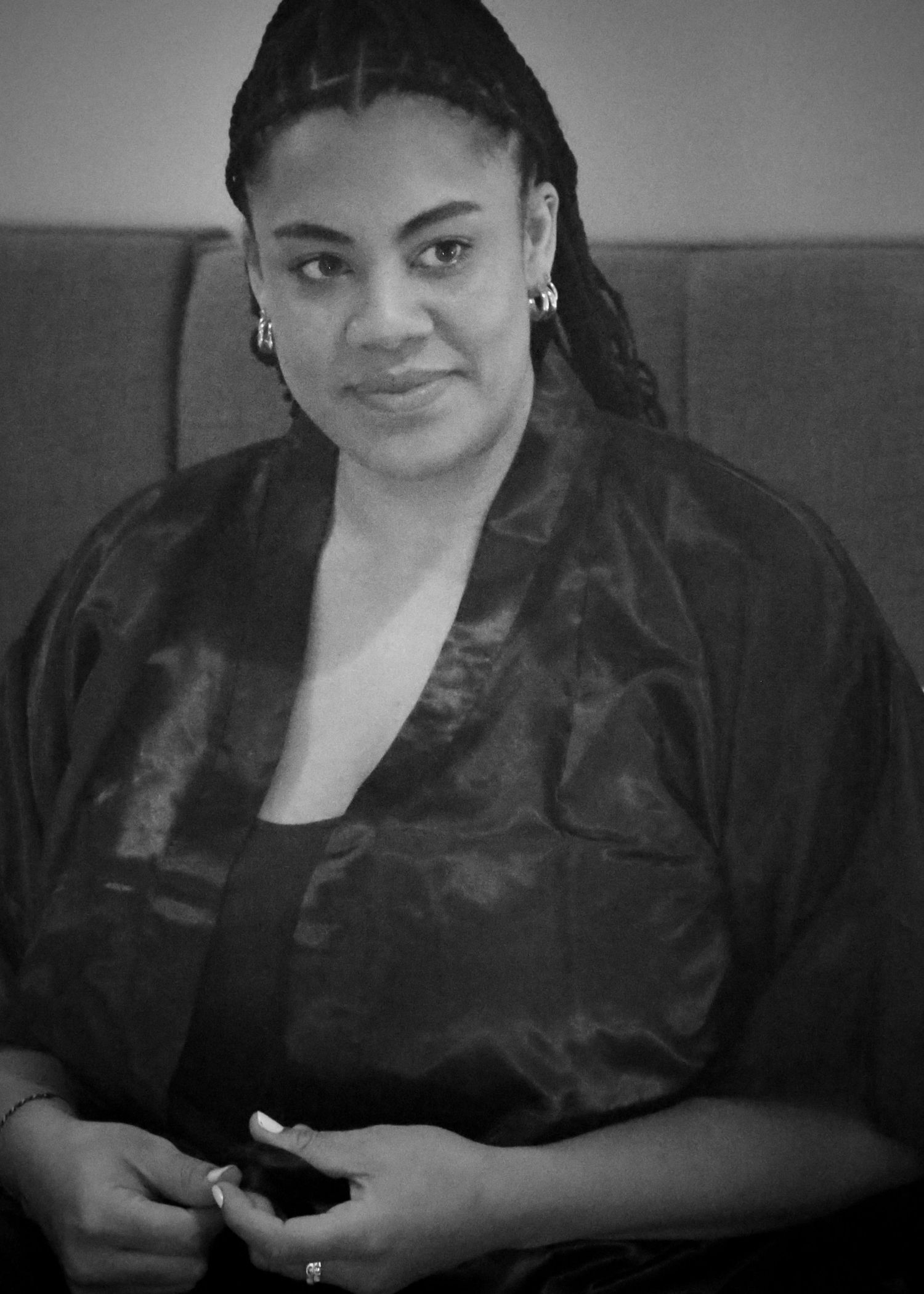 Portrait of a woman in black satin jacket with braided hair against grey background.