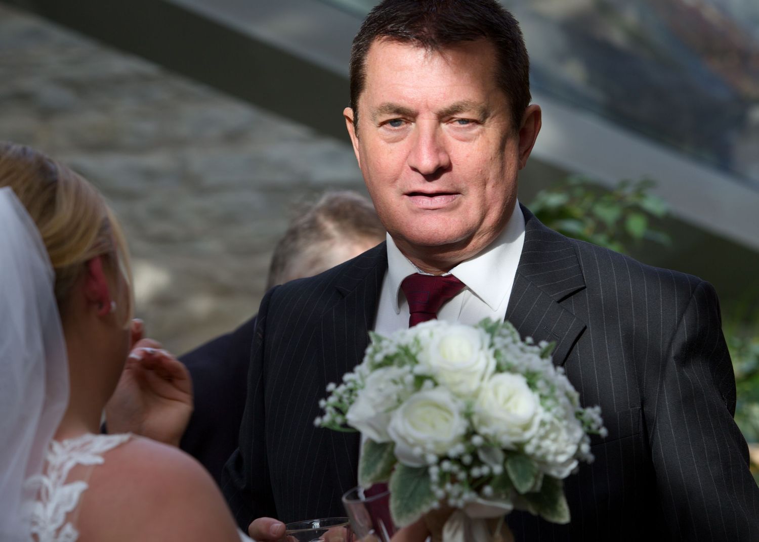 A guest at a formal event holds a white rose bouquet.