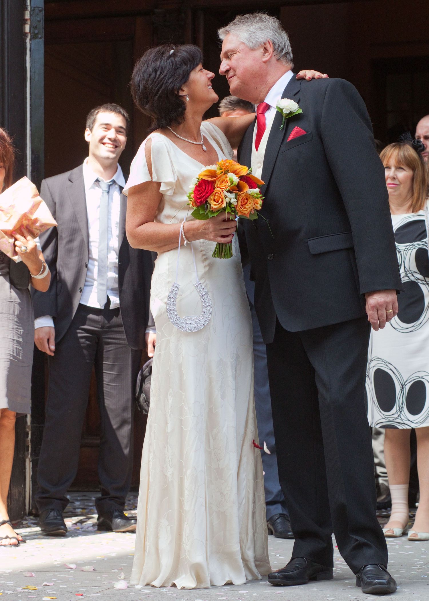 A wedding couple sharing an intimate moment outside while guests look on.