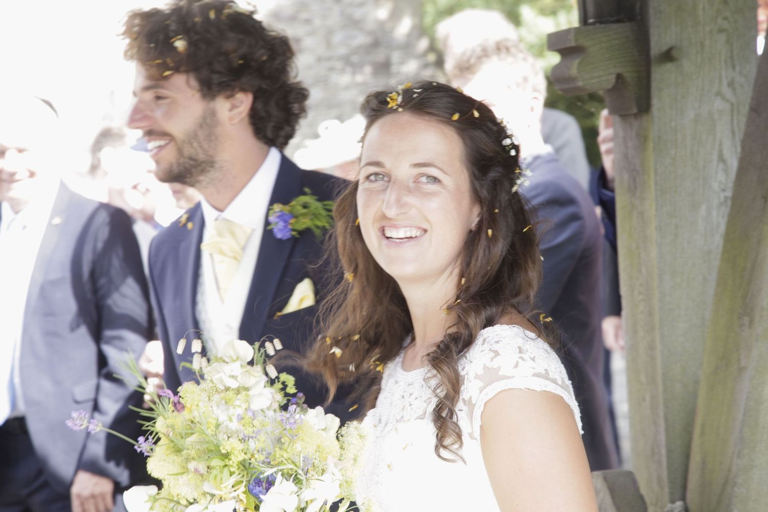 Happy wedding celebration with guests throwing confetti in garden setting.
