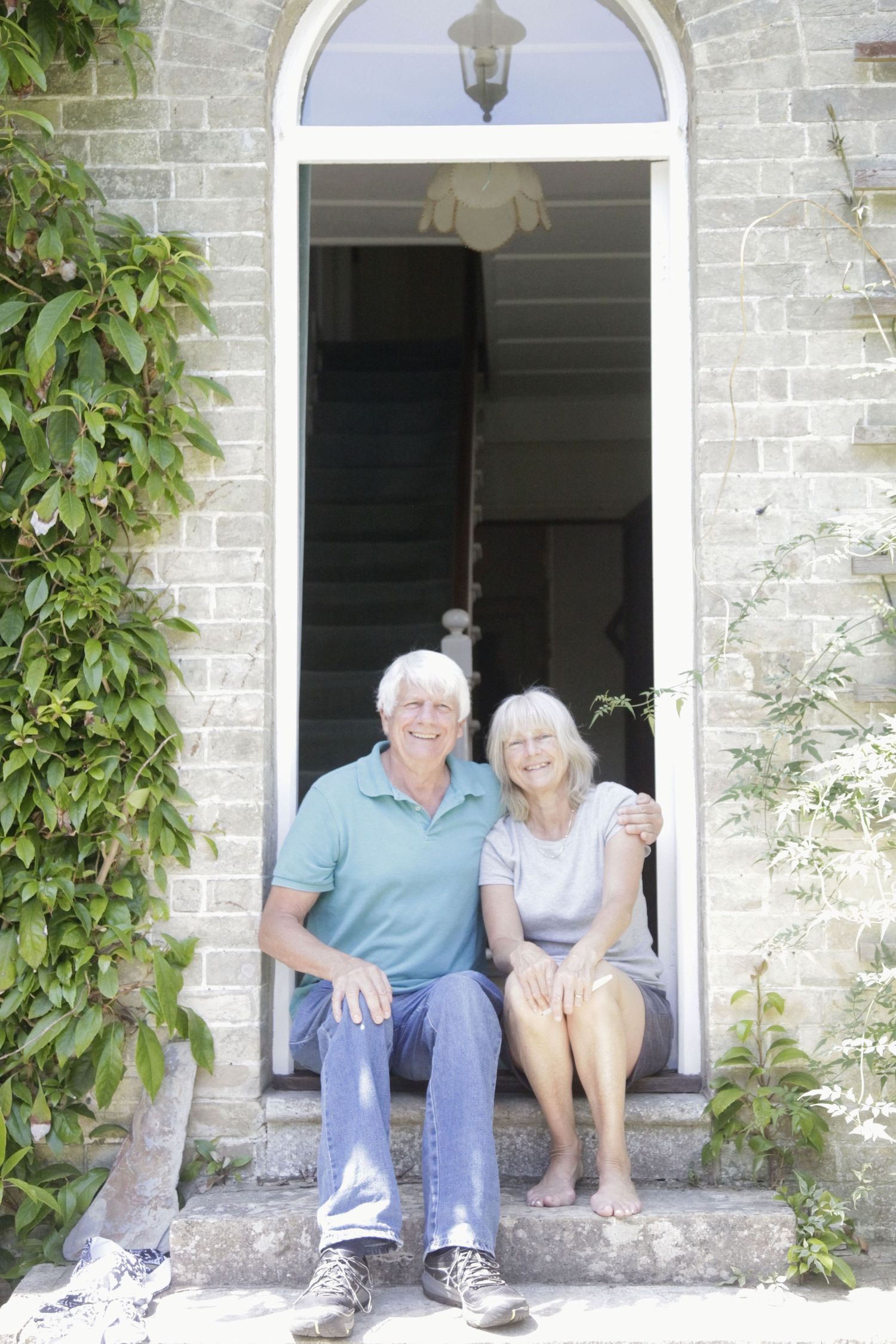 Elderly couple relaxing on stone steps with climbing vines framing the entrance.