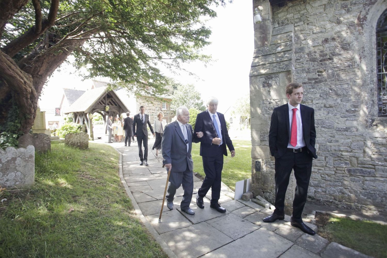 Formal wedding party walking along a stone path outside a traditional church entrance.