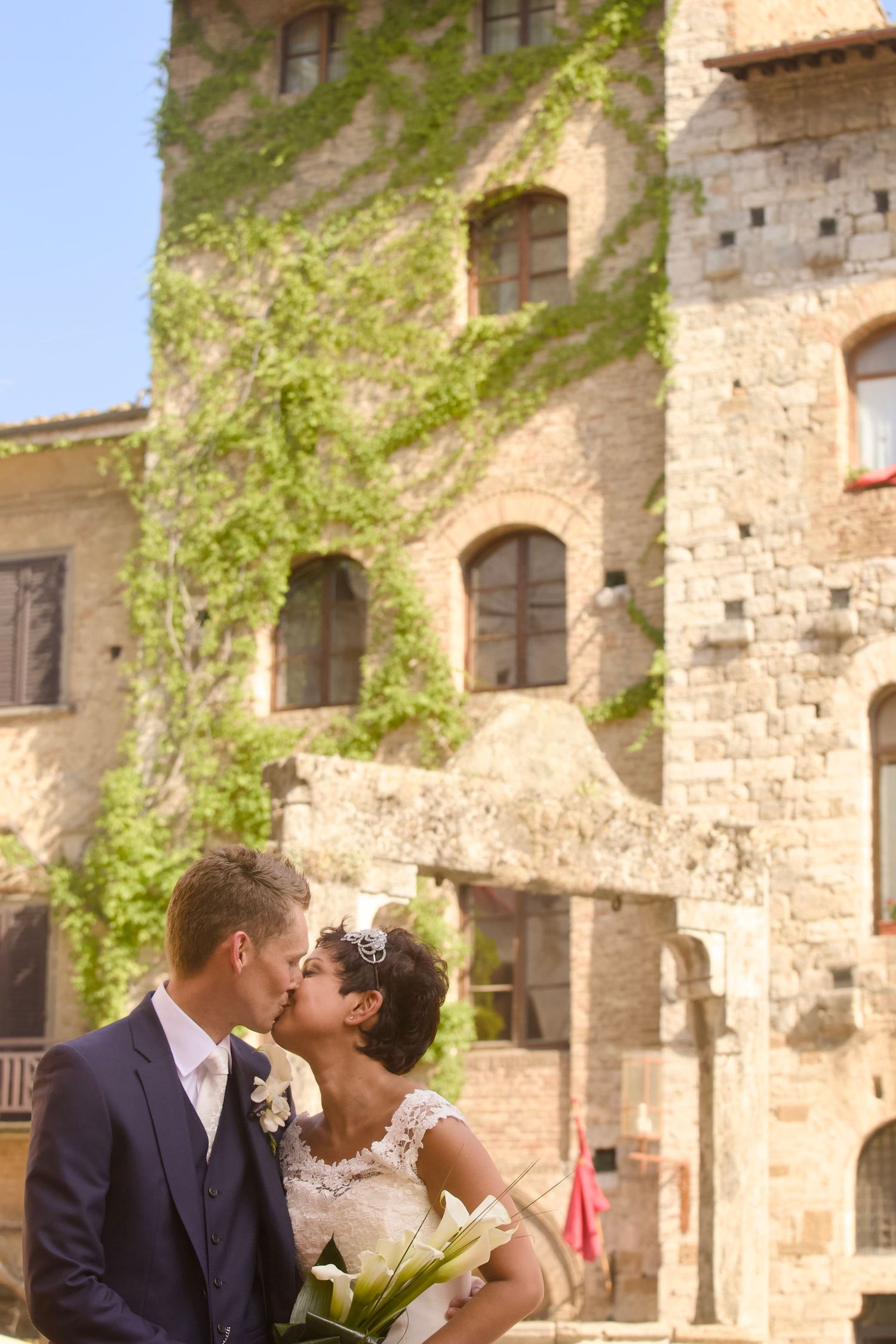 Romantic couple sharing a tender moment in front of a historic stone building with arched windows and climbing vines.