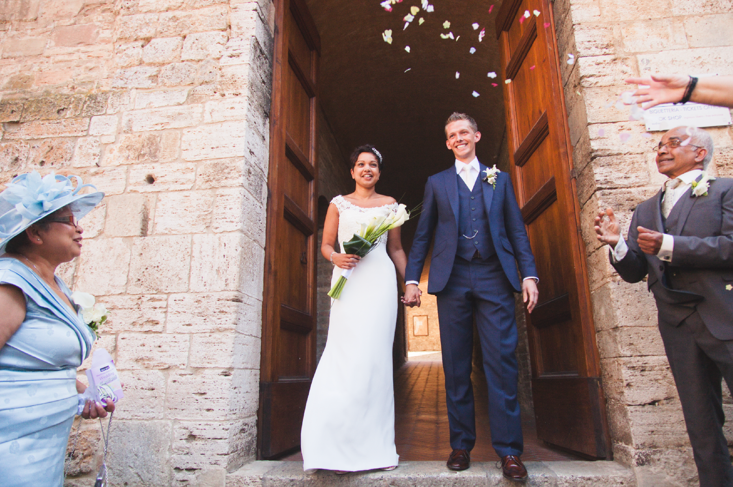 Confetti shower celebration outside historic brick church entrance during wedding.