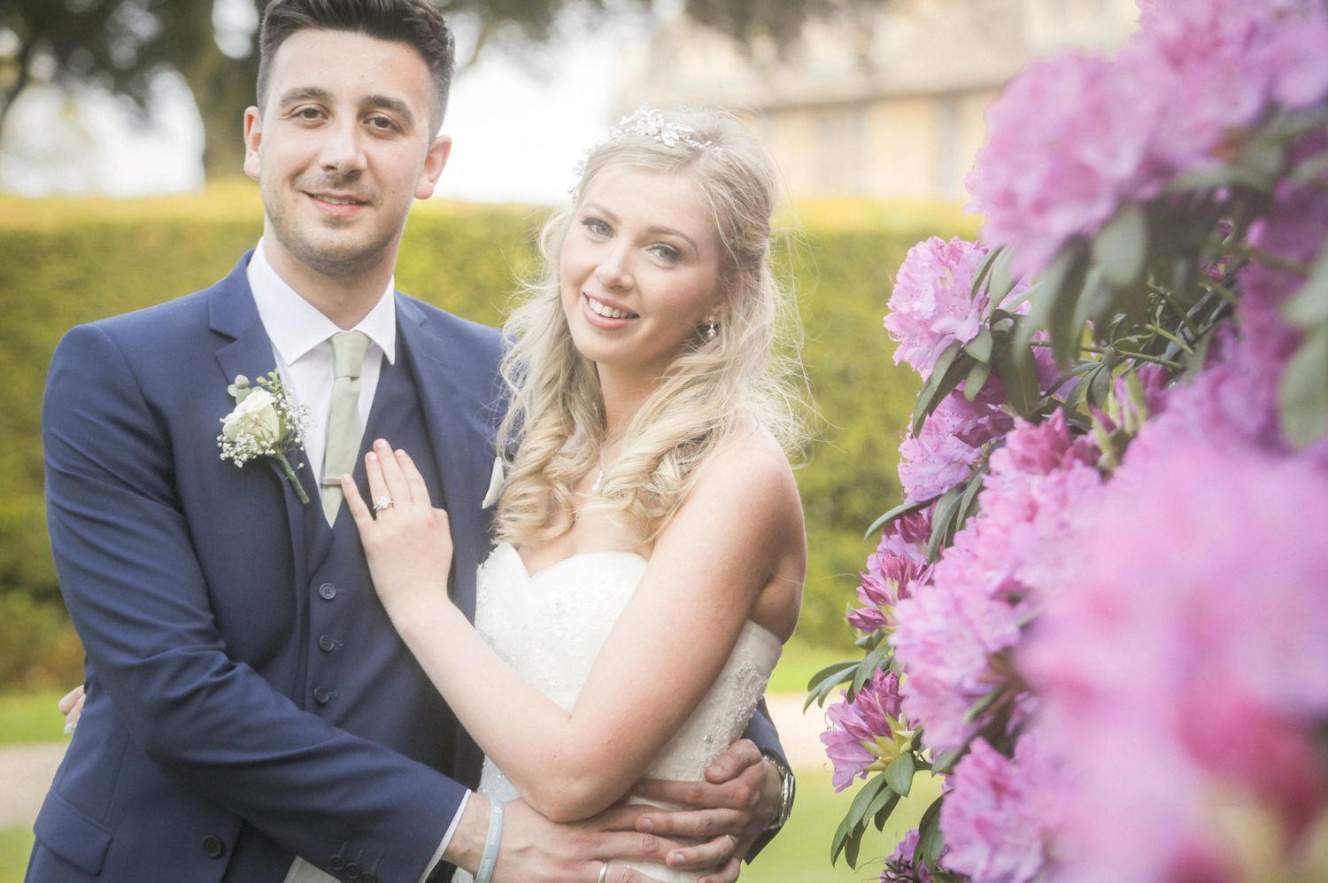 Wedding portraits with pink flowers in foreground at outdoor garden setting.