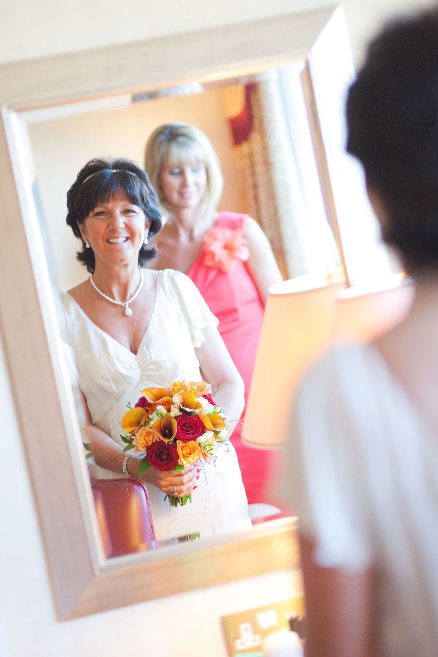 Joyful bride holding a vibrant orange and red bouquet while getting ready in a bright indoor setting.