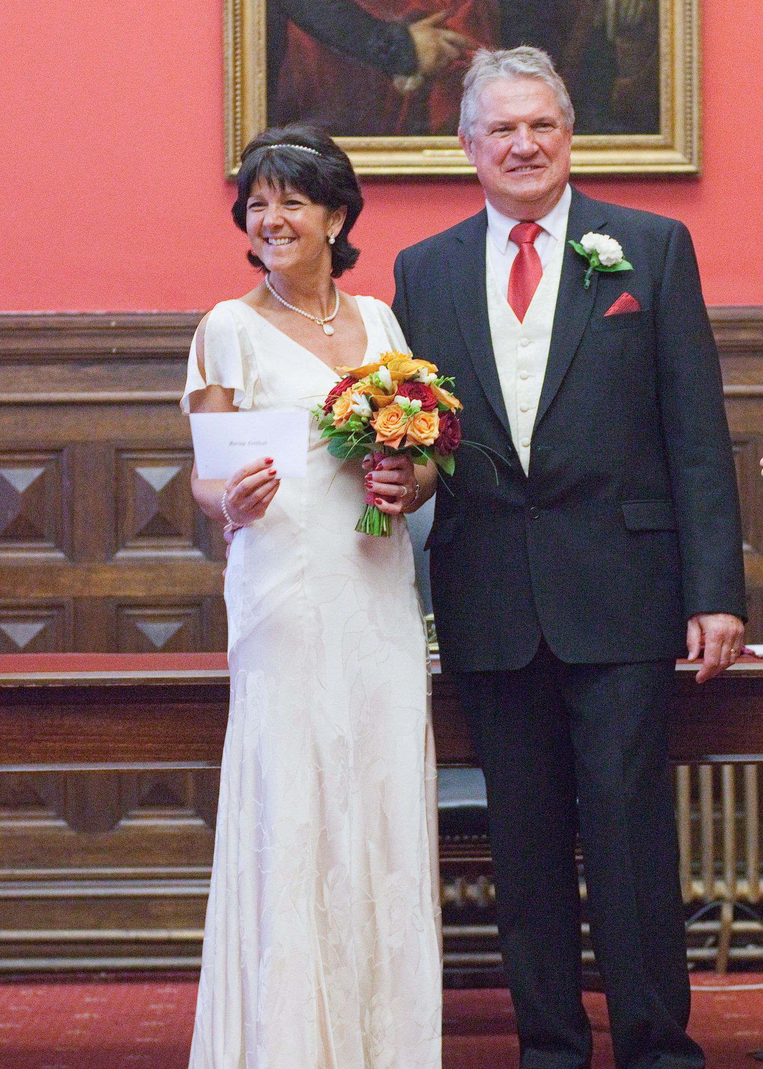 Wedding ceremony in formal room with traditional portraits and coral-colored walls.