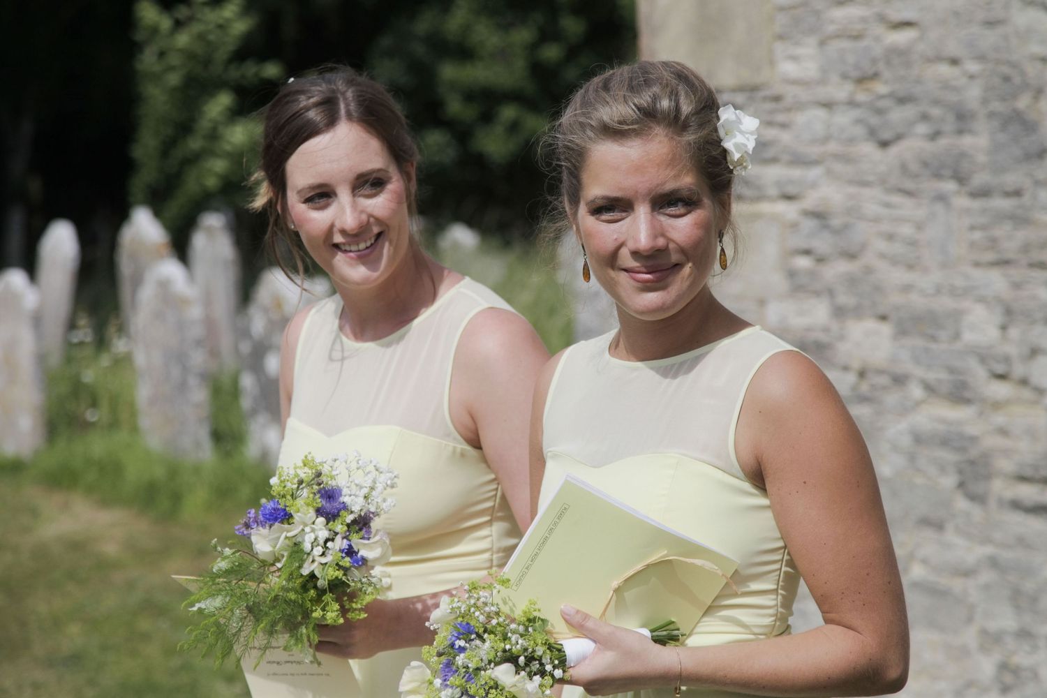 Bridesmaids in light yellow dresses pose together against a stone wall backdrop.