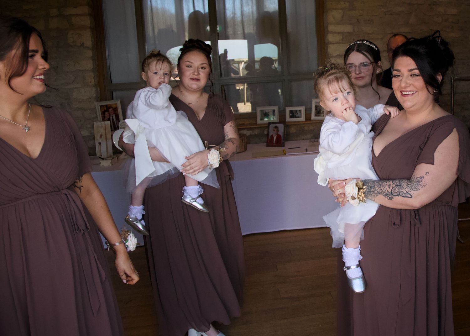 Wedding party members in brown dresses interact with small children in white outfits.