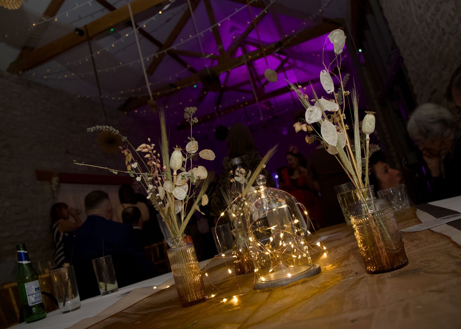 Elegant wedding reception table settings with glowing vases and purple uplighting create a romantic atmosphere.