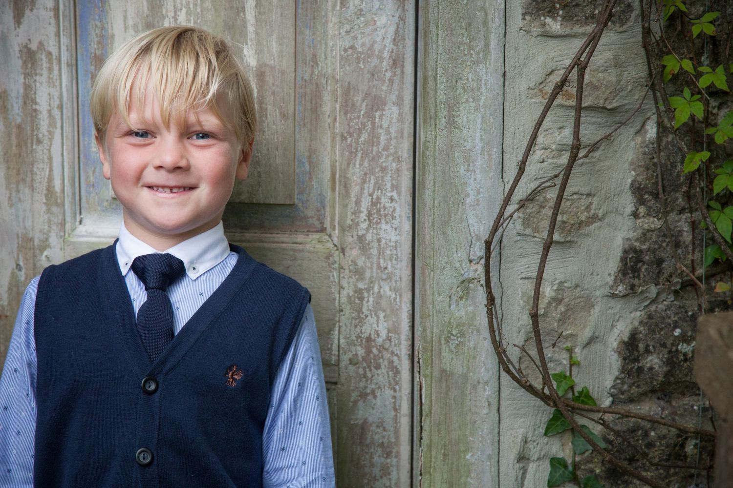 Children in formal attire pose against weathered wooden fence background.
