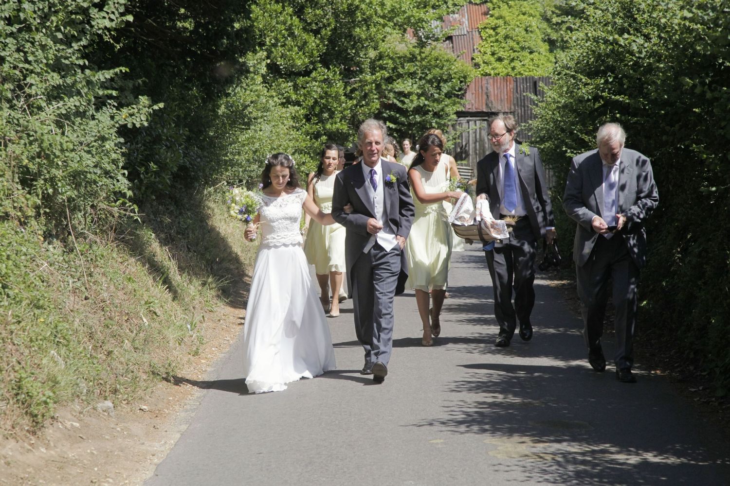 Wedding party walking up a tree-lined path during an outdoor ceremony.