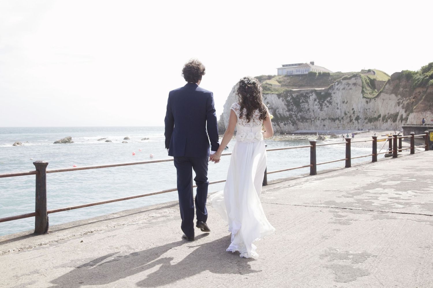 Wedding couple walking along coastal path with ocean views and metal railing.