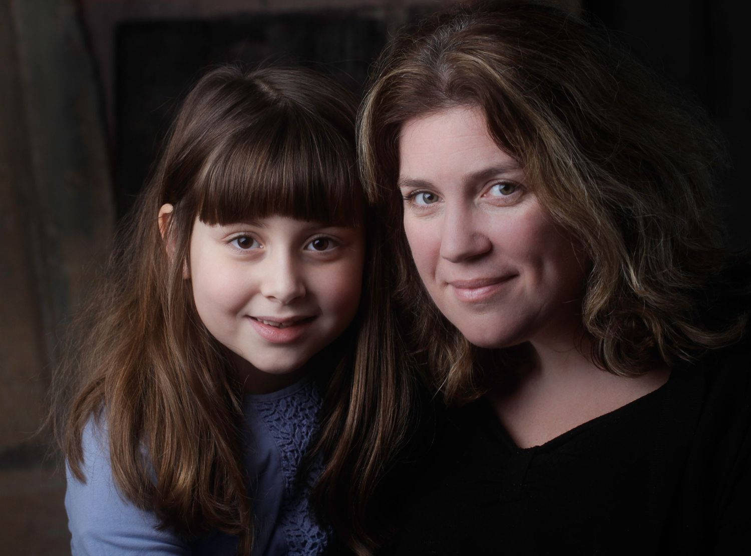 A portrait of a parent and child with brown hair against a dark background.
