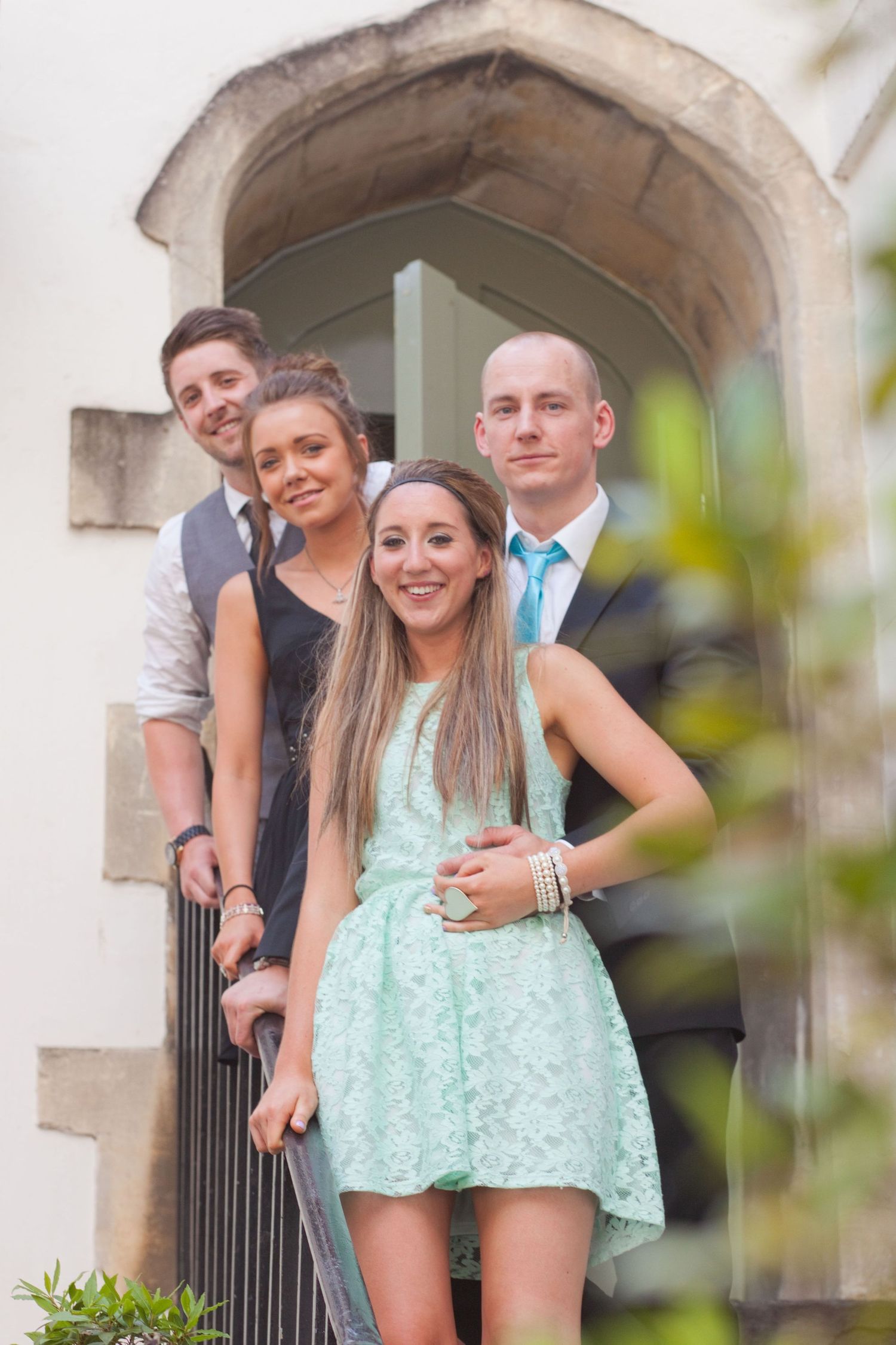 Group poses together on stone steps in formal attire with one wearing a mint green dress.