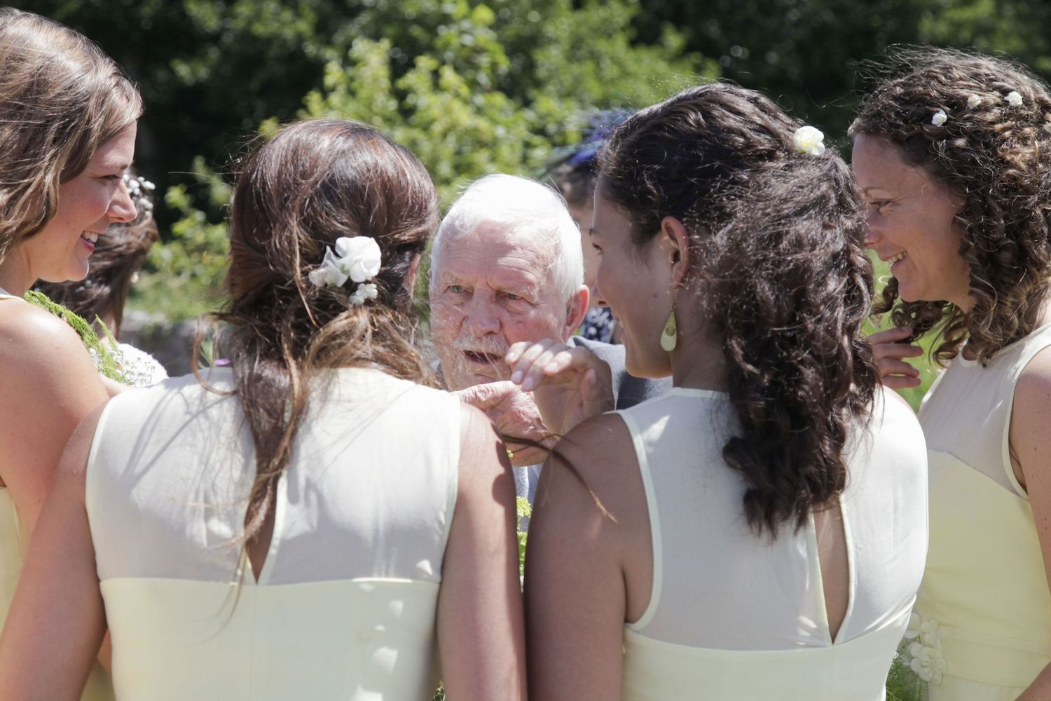 Wedding attendants in cream-colored dresses gather outdoors for group photos in a natural setting.